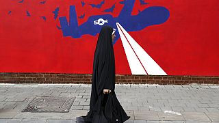 A woman walks past a new anti-U.S. mural on the wall of former US embassy in Tehran, 2019. 