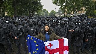 A woman holds a Georgian national and an EU flags in front of riot police