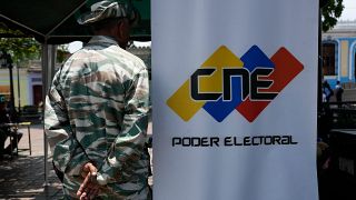 A Bolivarian Militia member stands guard next to a banner of the National Electoral Council where people can register to vote in Caracas, Venezuela.