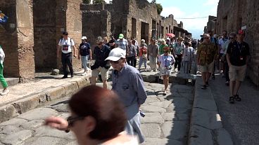 Visitors walk down an ancient Roman street in the Pompeii archeological site