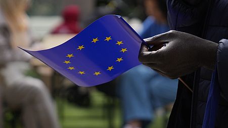 A man holds a European Union flag as he walks outside the European Commission building during Europe Day celebrations in Brussels on May 4, 2024.